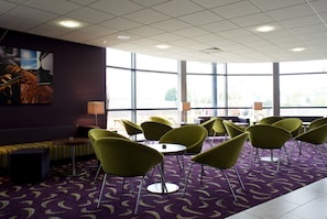 Un hall d’hôtel avec un tapis violet, des fauteuils verts, un canapé et de grandes fenêtres.