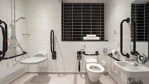 Et moderne badeværelse med en hvid vask, toilet og brusebad. Der er gelænder og et vindue over toilettet.