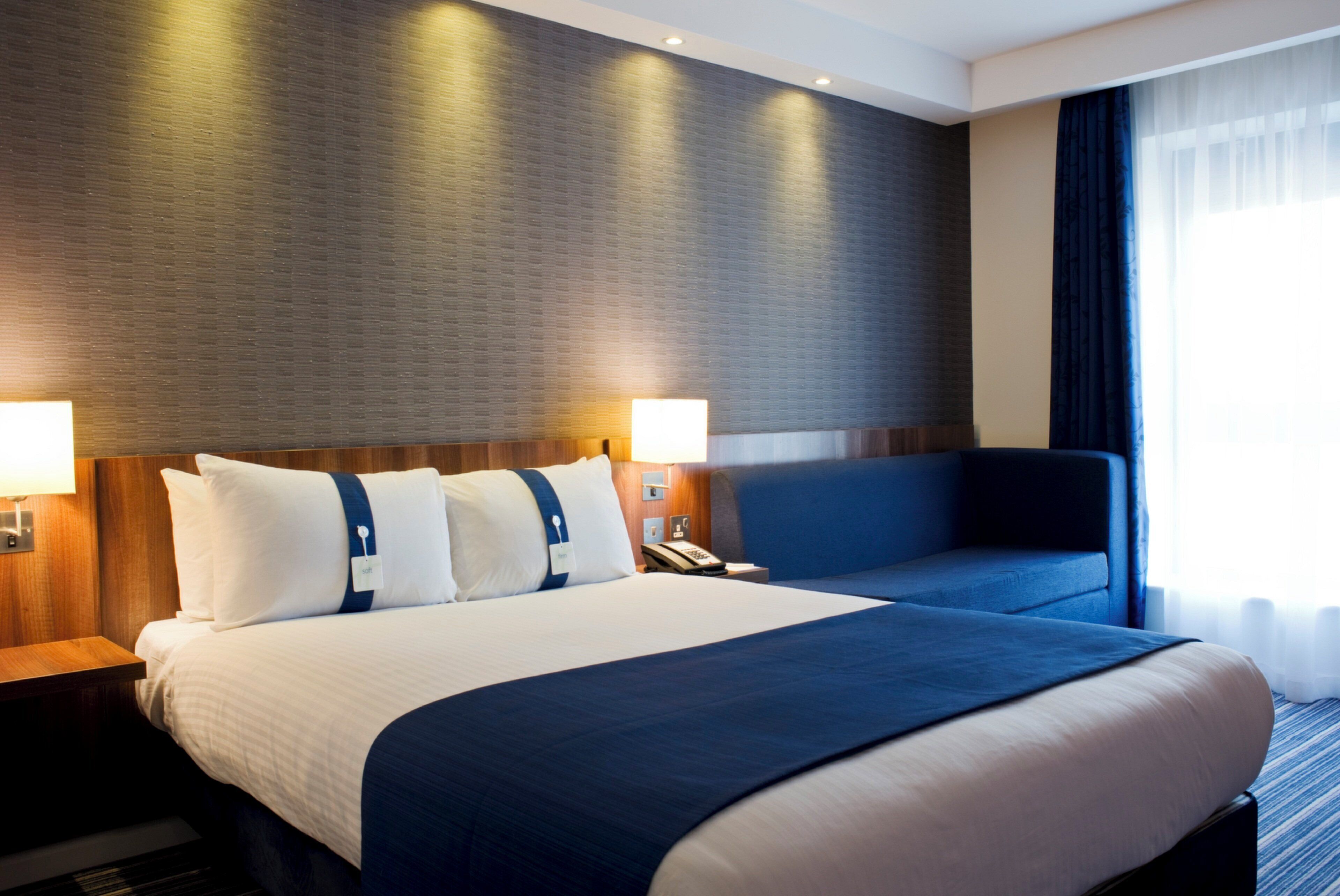 Une chambre d’hôtel avec un grand lit, deux tables de chevet, un bureau, une chaise et une fenêtre avec des rideaux.