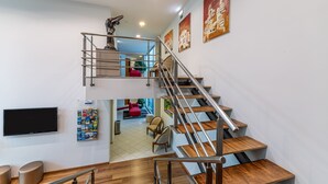 A modern interior with a wooden staircase, a flat-screen TV, and a seating area with a red chair. - Hotel Sao Sebastiao de Boliqueime (Loulé)