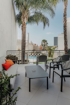 A balcony with a white sofa, a table, and chairs, overlooking a swimming pool and buildings. - Hotel Sao Sebastiao de Boliqueime (Loulé)
