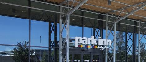 Un edificio moderno con un amplio frente de vidrio, techo de listones de madera y un letrero que dice "Park Inn".