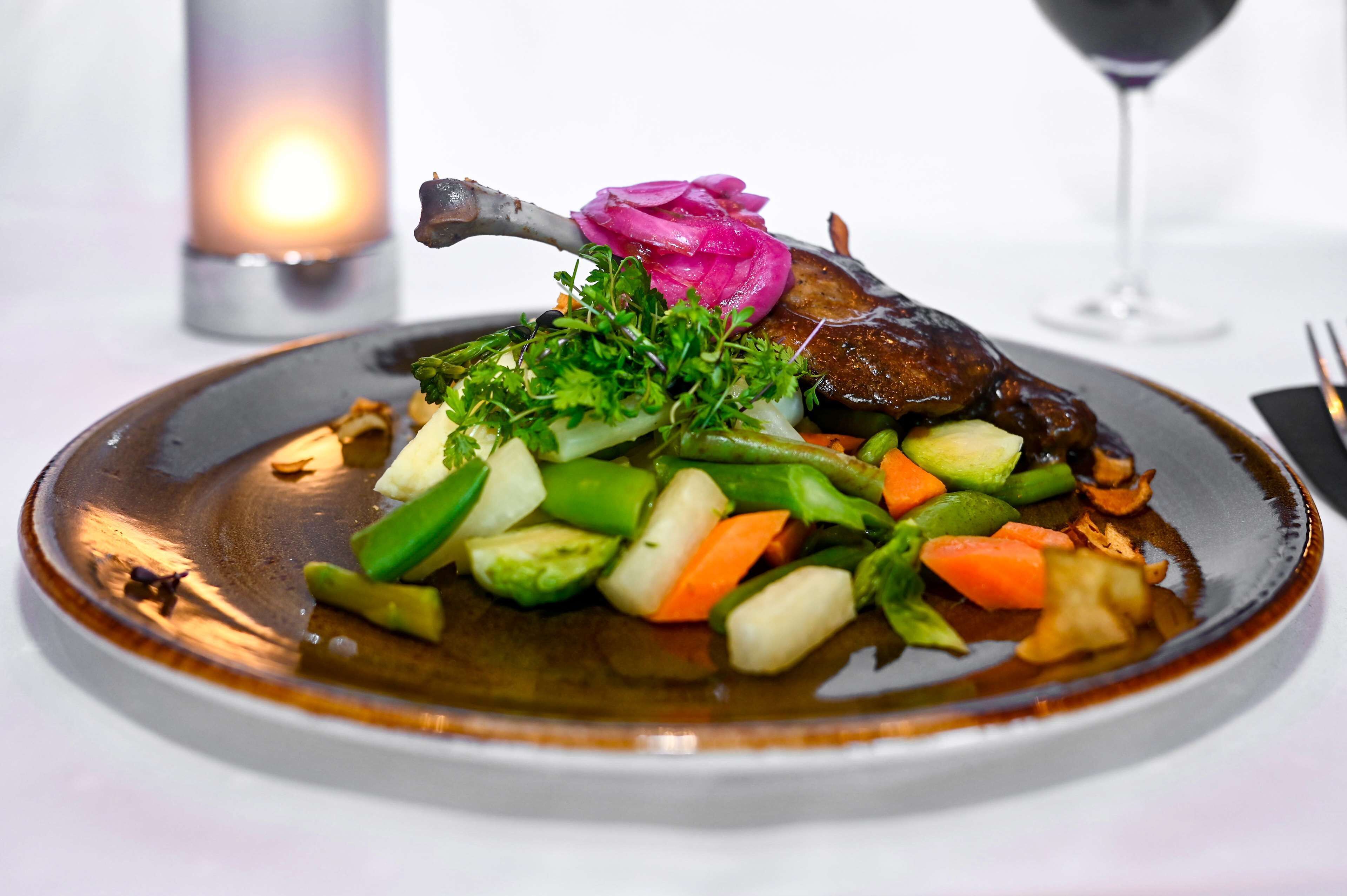 A plate of food with a duck leg, vegetables, and a decorative flower.