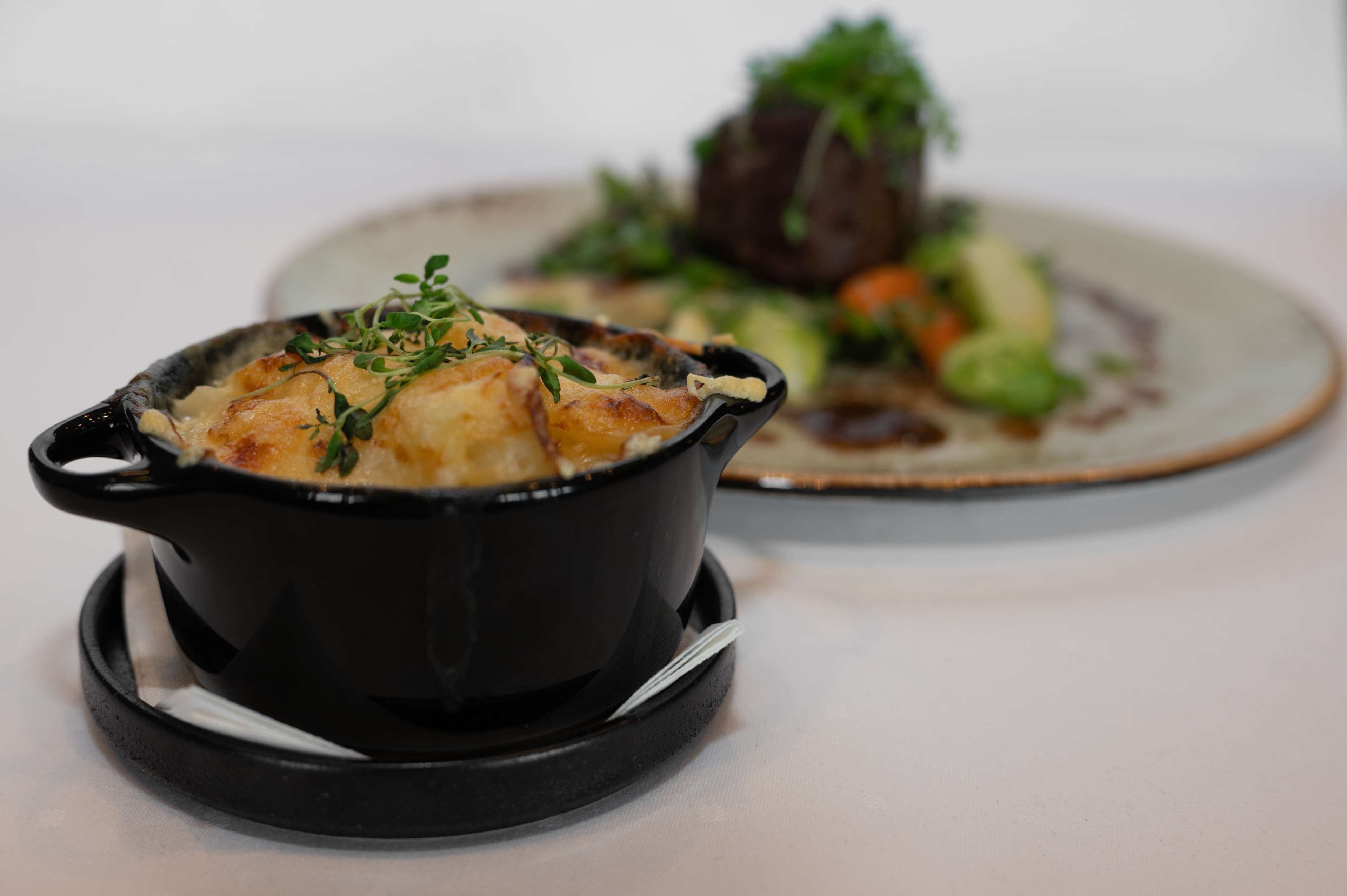 A black pot on a white table with a plate of food in the background.