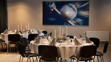 A dining area with round tables set for a meal, featuring white tablecloths, candles, and a large painting of a space scene on the wall.