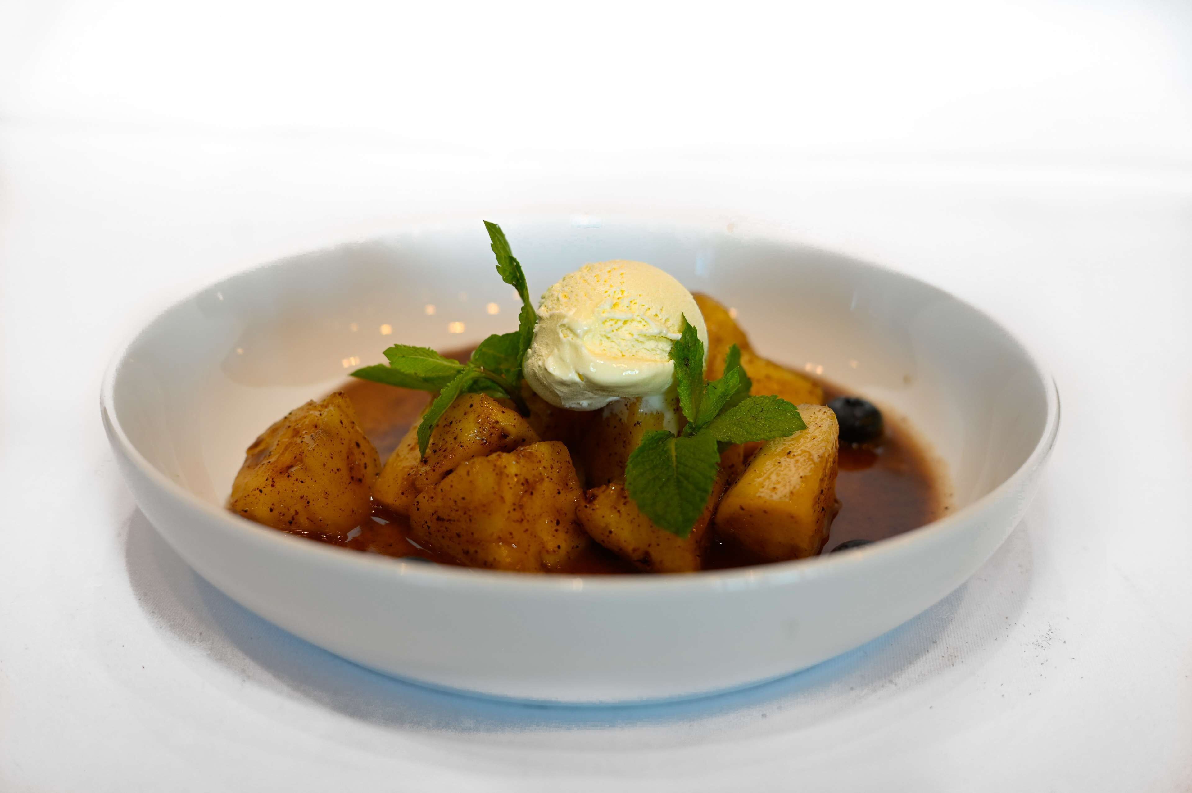 Un dessert agrémenté d’une boule de glace, décoré de feuilles de menthe et servi dans un bol blanc.