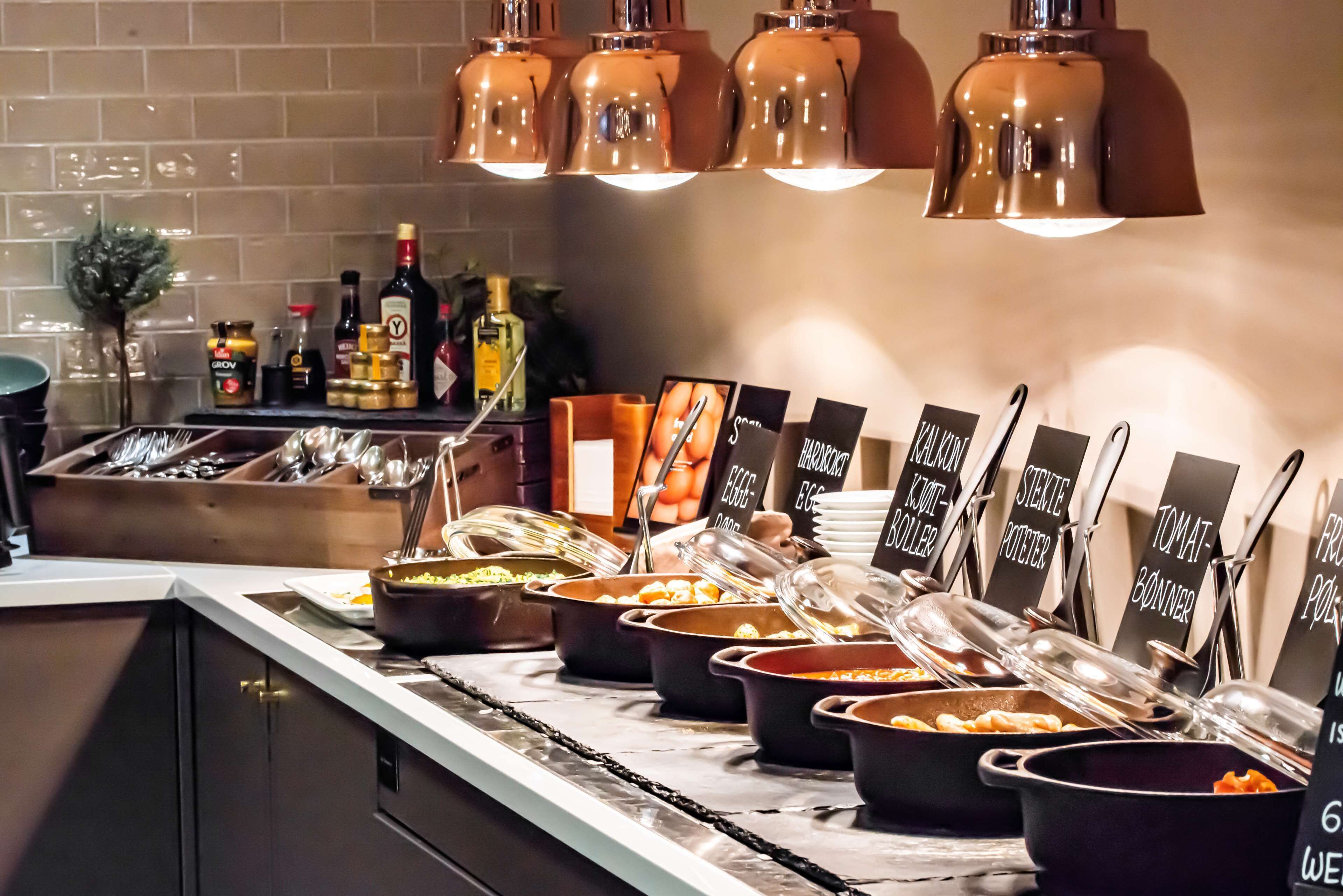 A buffet setup with various food items and utensils, including labeled containers for different dishes.