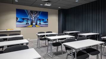 Une salle de conférence avec des tables blanches et des chaises noires, un grand tableau représentant un avion accroché au mur et un mur lambrissé de couleur sombre.