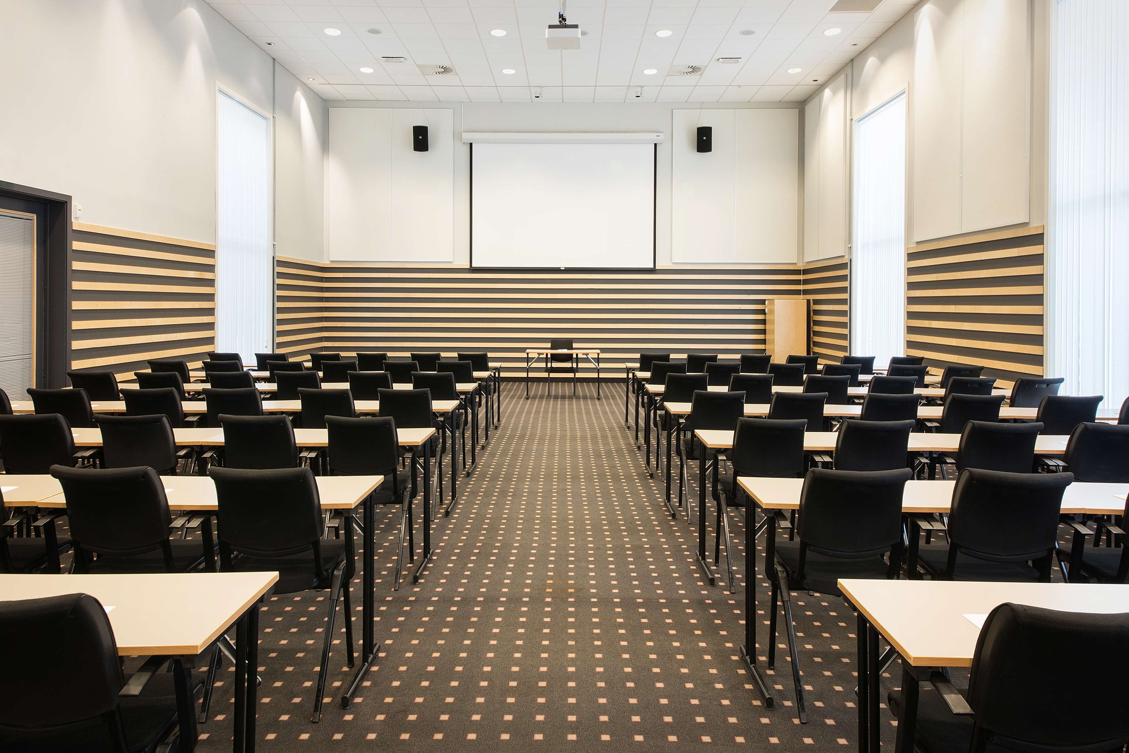 A conference room with rows of tables and chairs, a projector screen, and a large window.
