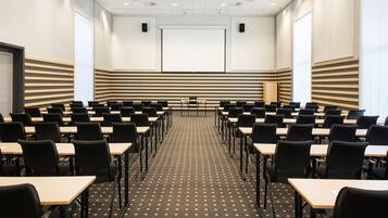 A conference room with rows of tables and chairs, a projector screen, and a large window.