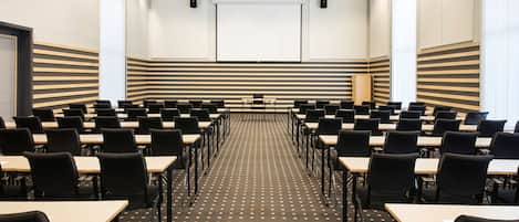 A conference room with rows of tables and chairs, a projector screen, and a large window.