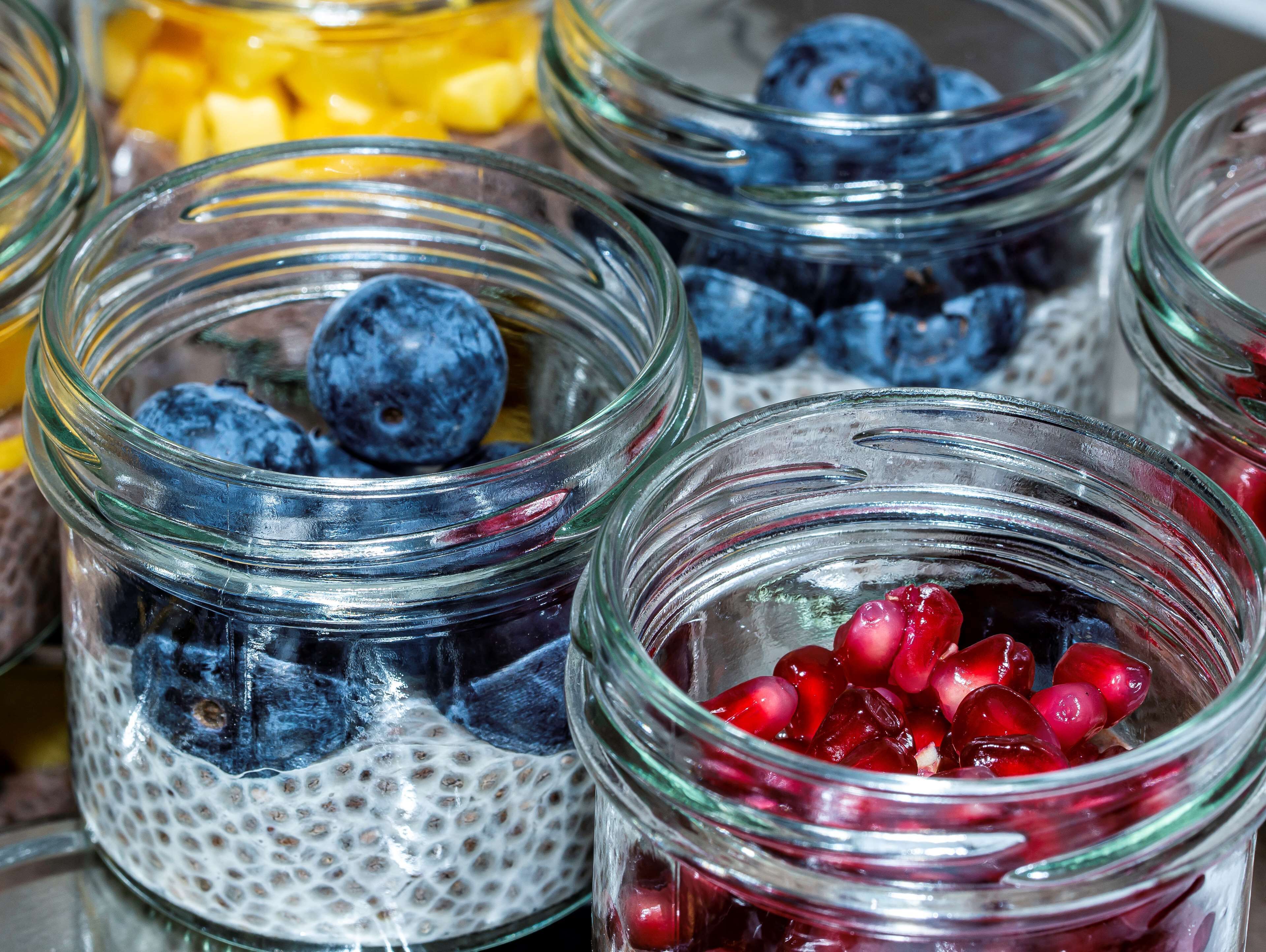 A close-up of glass jars containing chia seeds, blueberries, and pomegranate seeds.