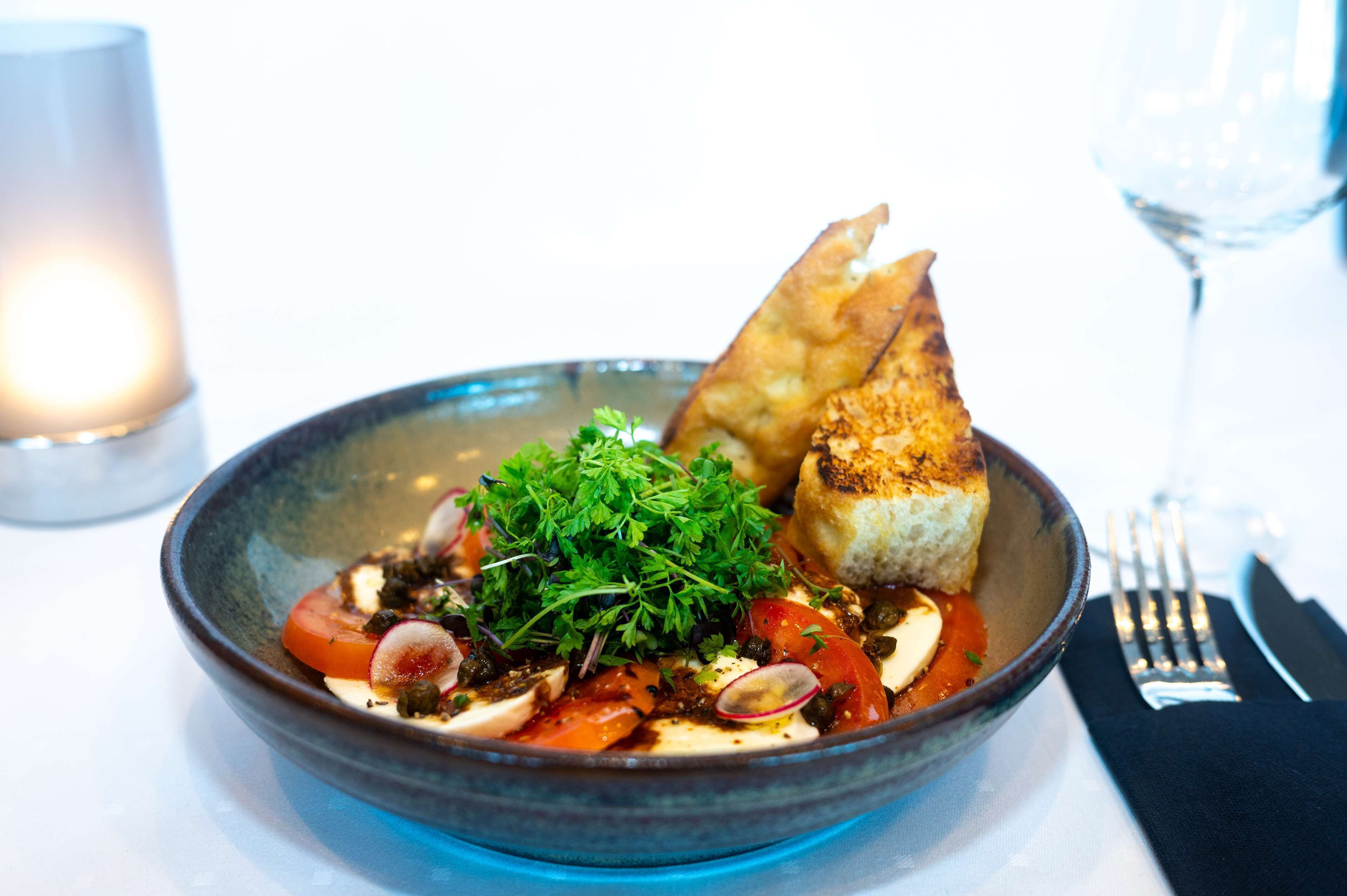 A bowl of food with a piece of bread and a glass of water on a table.