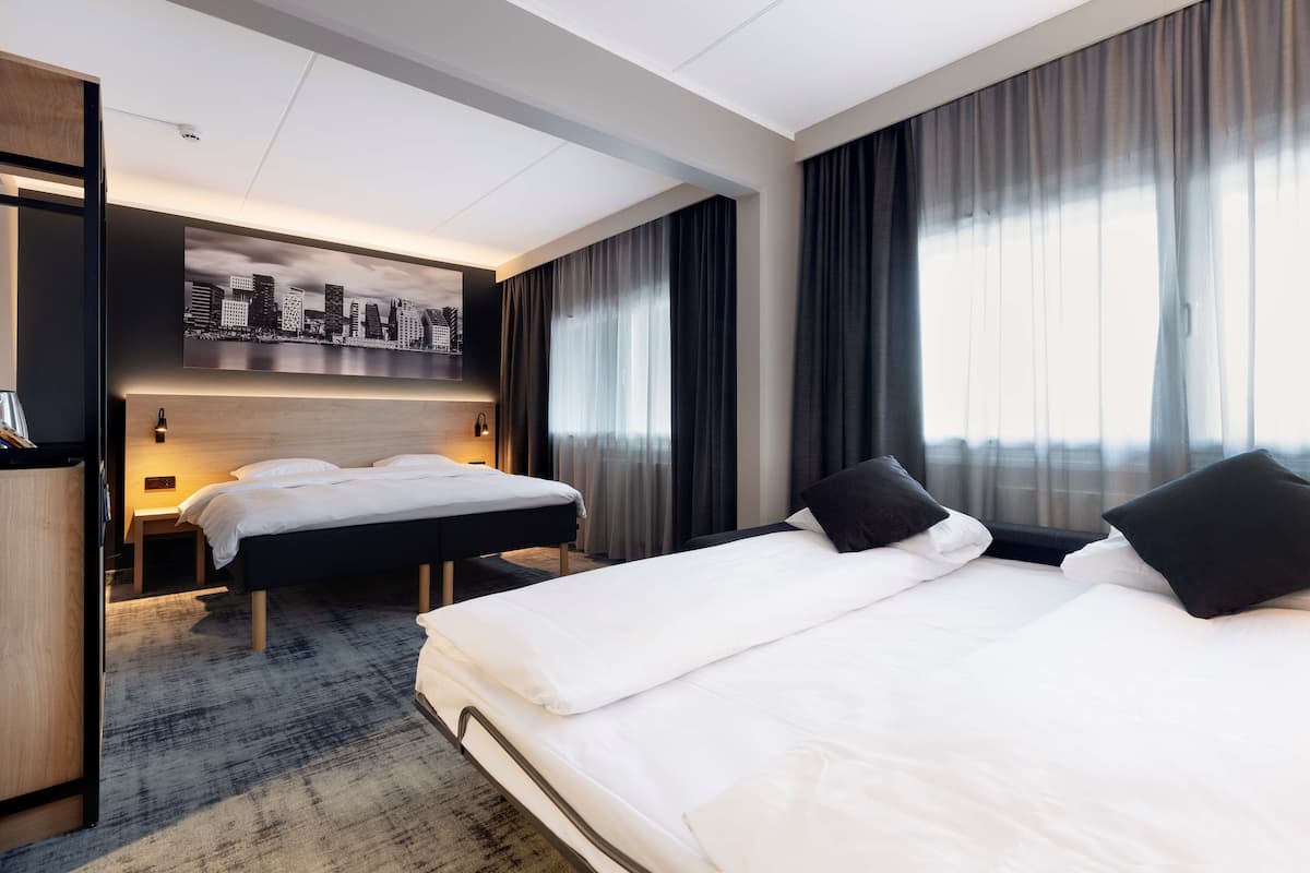 Una habitación de hotel con dos camas, una obra de arte con un paisaje urbano en la pared y un ventanal con cortinas.