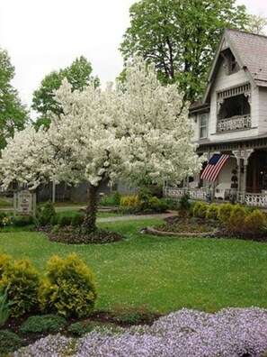 A two-story house with a porch and a large white flowering tree in the front yard.