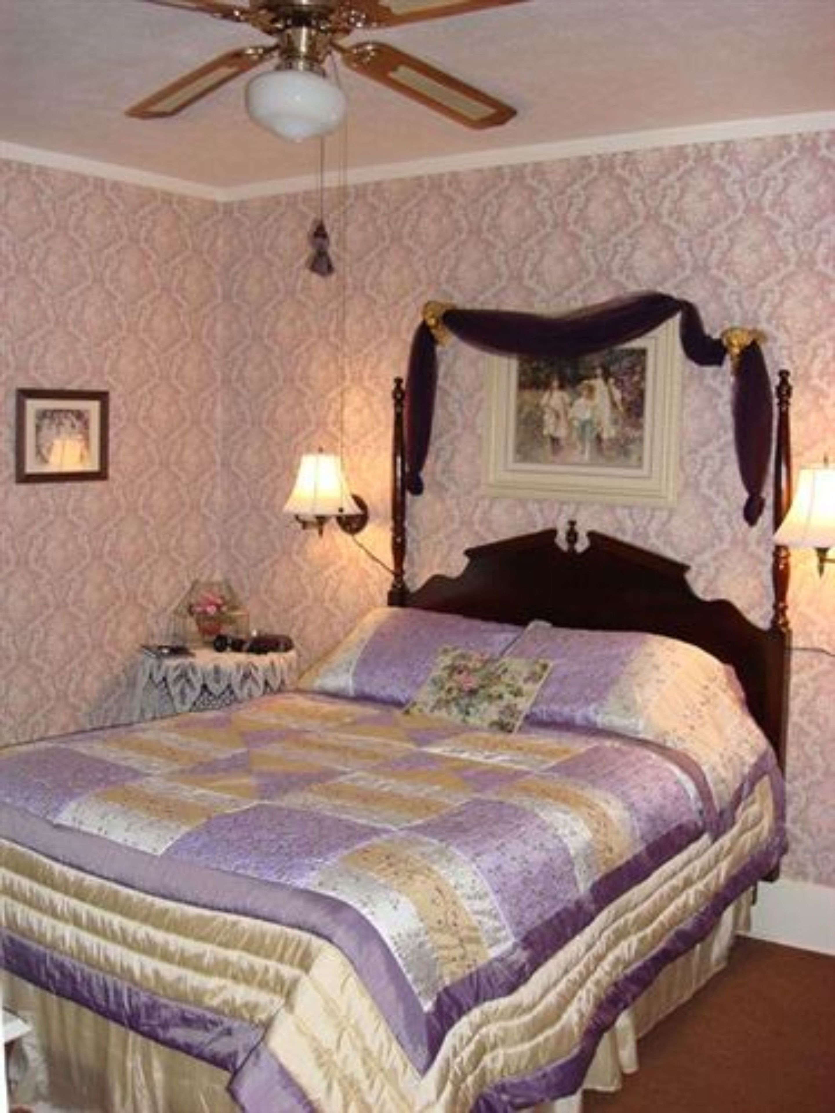 A bedroom with a four-poster bed, a ceiling fan, and two bedside lamps.