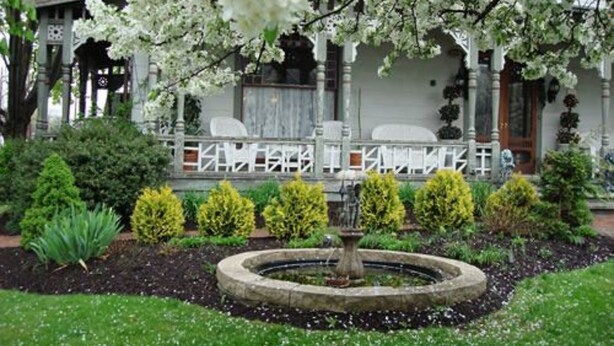 A garden with a fountain, neatly trimmed hedges, and a gazebo.