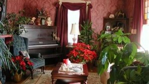 A cozy living room with a piano, a coffee table, and various plants.