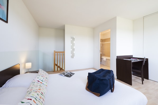 Una habitación de hotel moderna con cama, escritorio y zona de ducha.