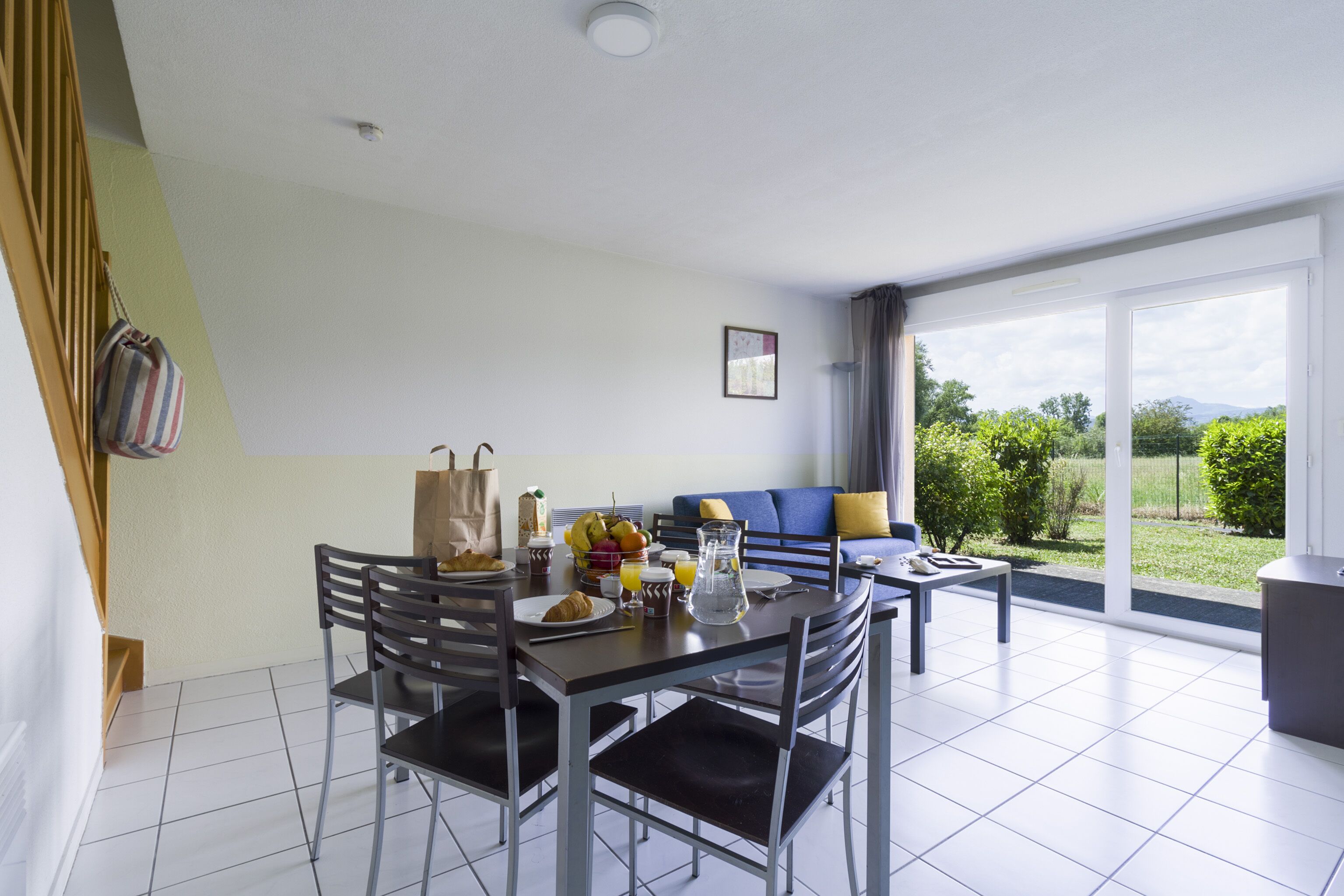 A modern dining area with a table set for breakfast, a sofa, and a view of the outdoors.