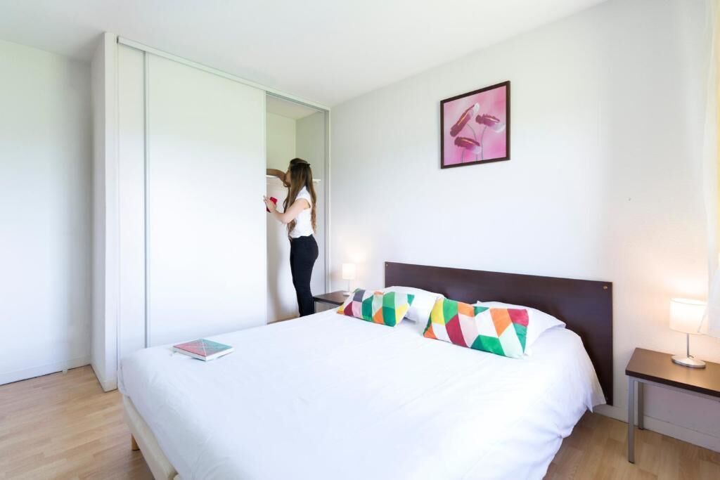 Une chambre d’hôtel avec un lit, une table de chevet, une lampe, un miroir et une porte.