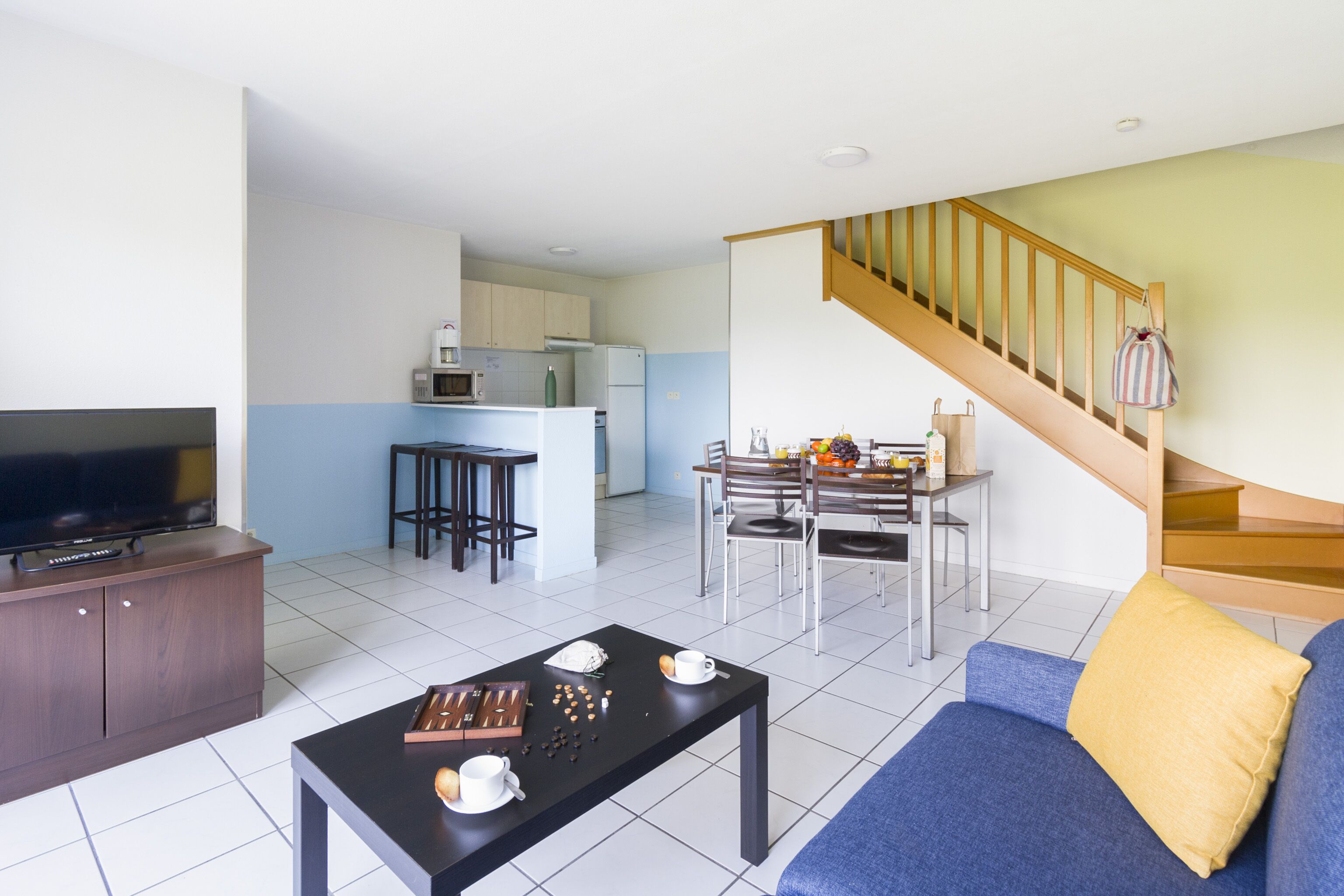 A modern living room with a sofa, a coffee table, and a TV. There is a staircase leading to an upper level.