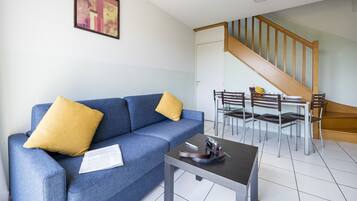 Ein Wohnzimmer mit einem blauen Sofa, gelben Kissen, einem kleinen Tisch und einer Treppe, die in einen Essbereich mit Stühlen und einem Tisch führt.