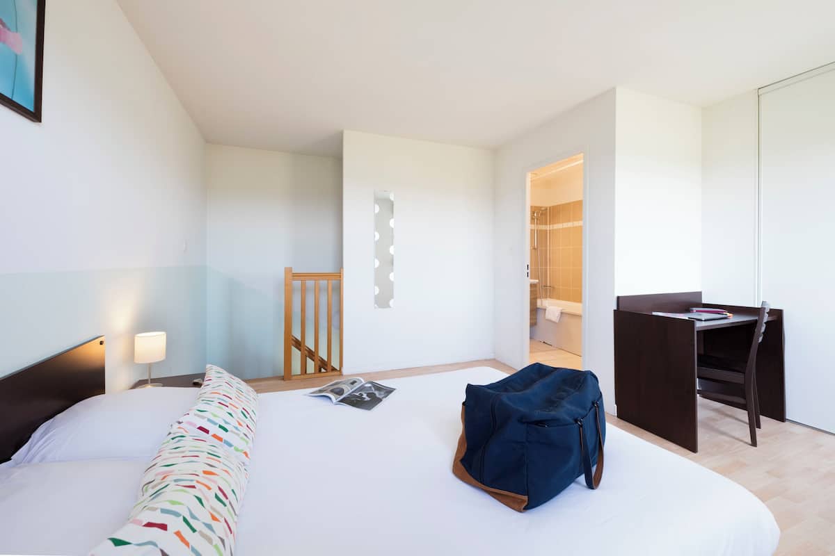 Une chambre d’hôtel moderne équipée d’un lit, d’un bureau et d’un espace douche.