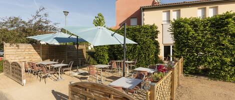 An outdoor patio area with tables and chairs, a wooden fence, and a building in the background.