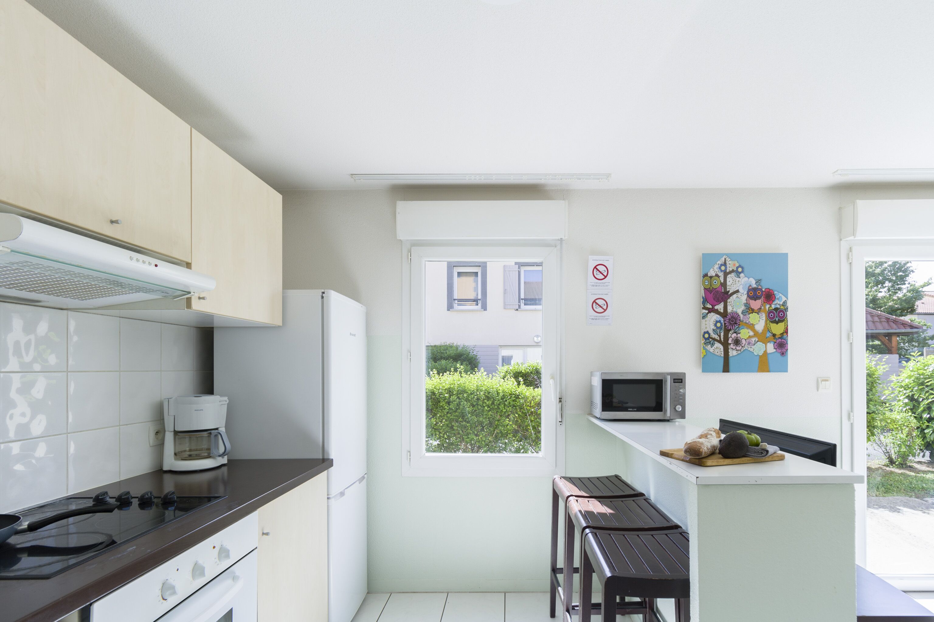 A compact kitchen with a stove, microwave, and coffee maker. There is a window with a view of greenery outside.