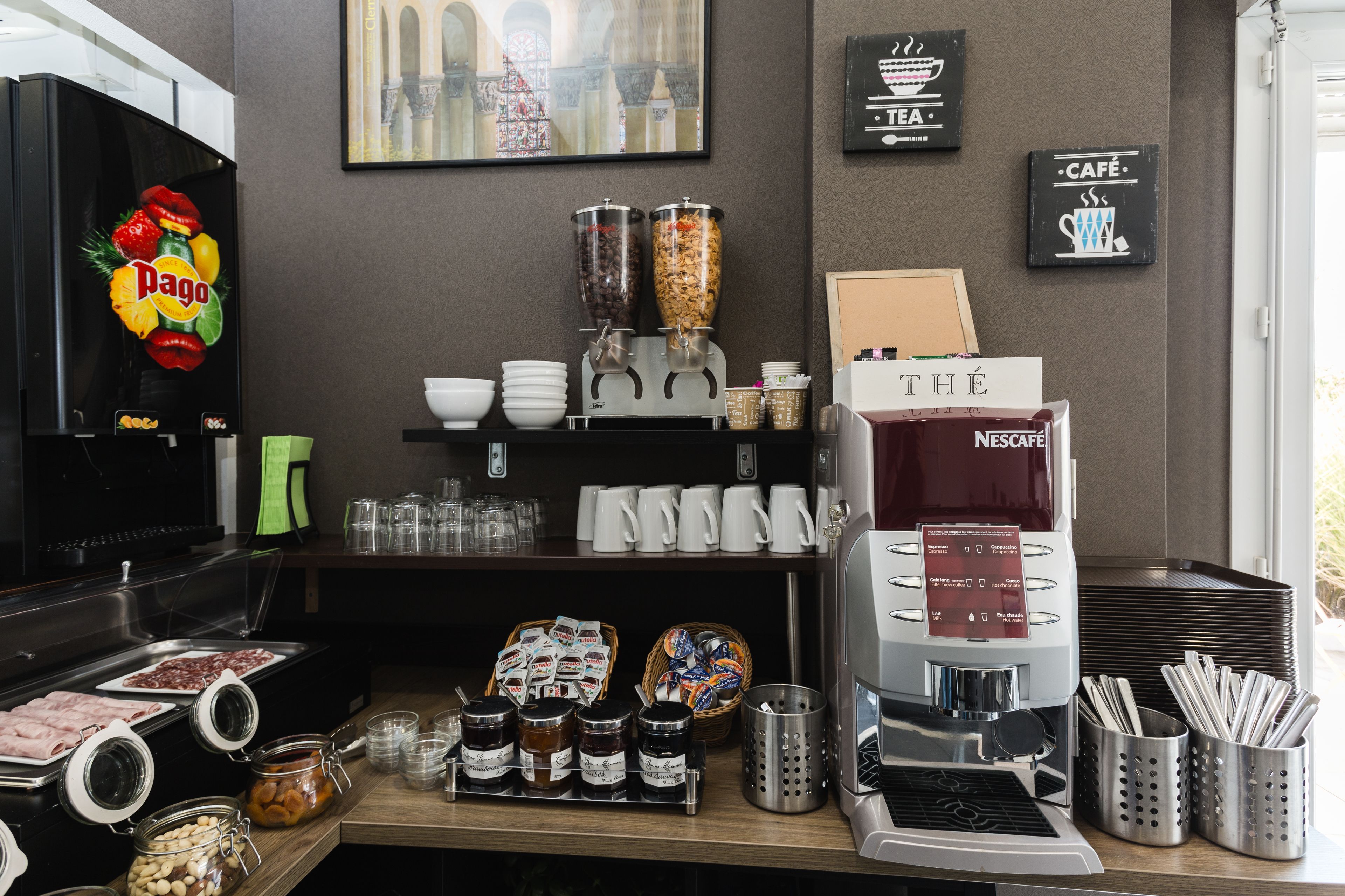 Una estación de café con máquina de Nescafé, frascos de condimentos y una cesta de pasteles.