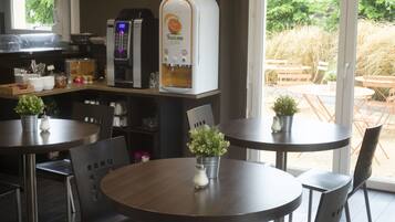 A cafe interior with round tables, chairs, a coffee machine, and a view of the outdoor seating area.