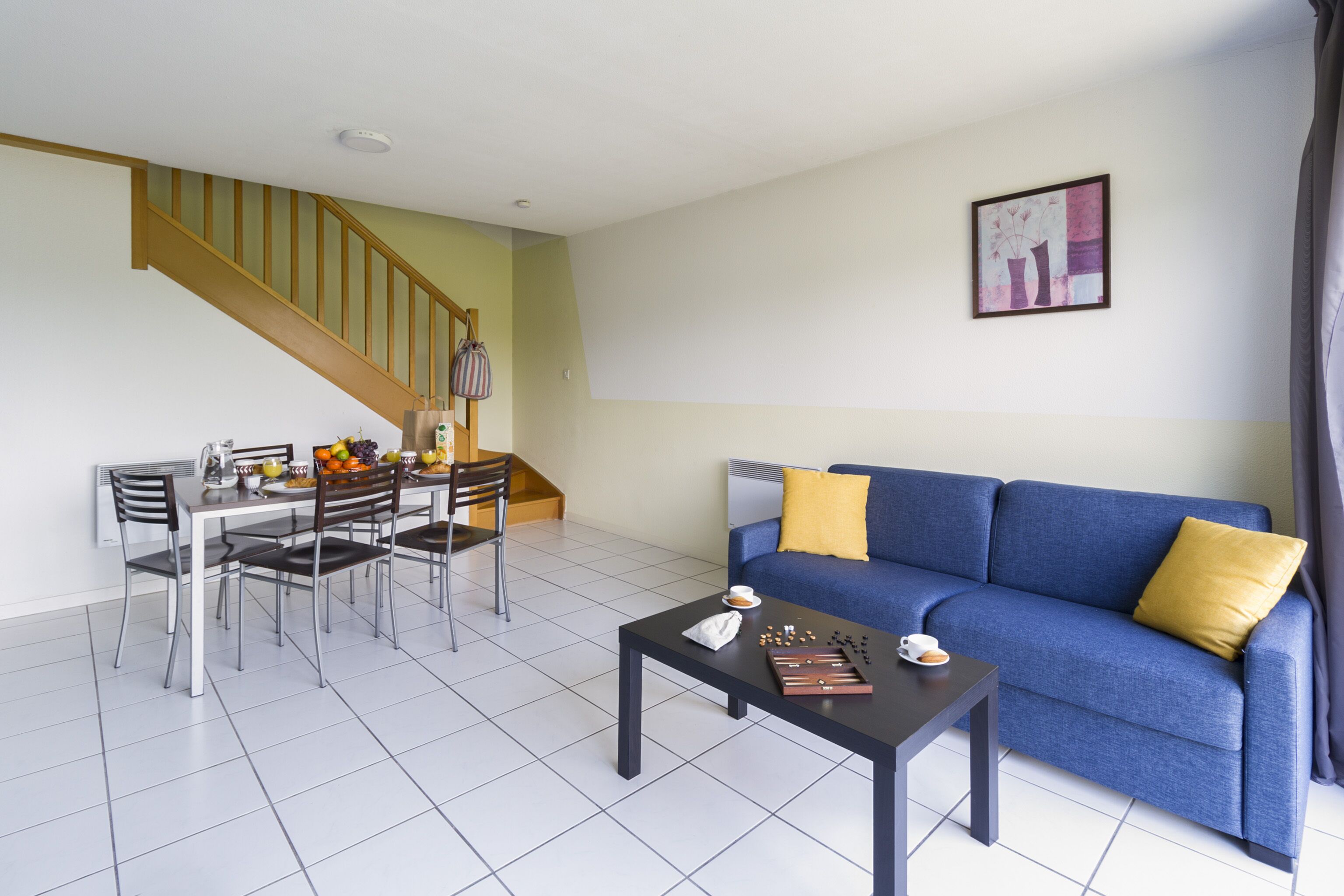 Ein Wohnzimmer mit einem blauen Sofa, einem Couchtisch und einem Essbereich mit Stühlen und einem Tisch.