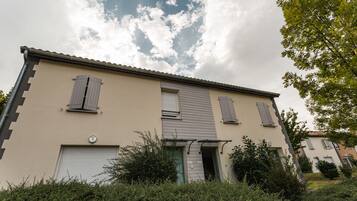Un bâtiment à deux étages, doté d’une façade beige, de volets aux fenêtres et d’une porte de garage visible.