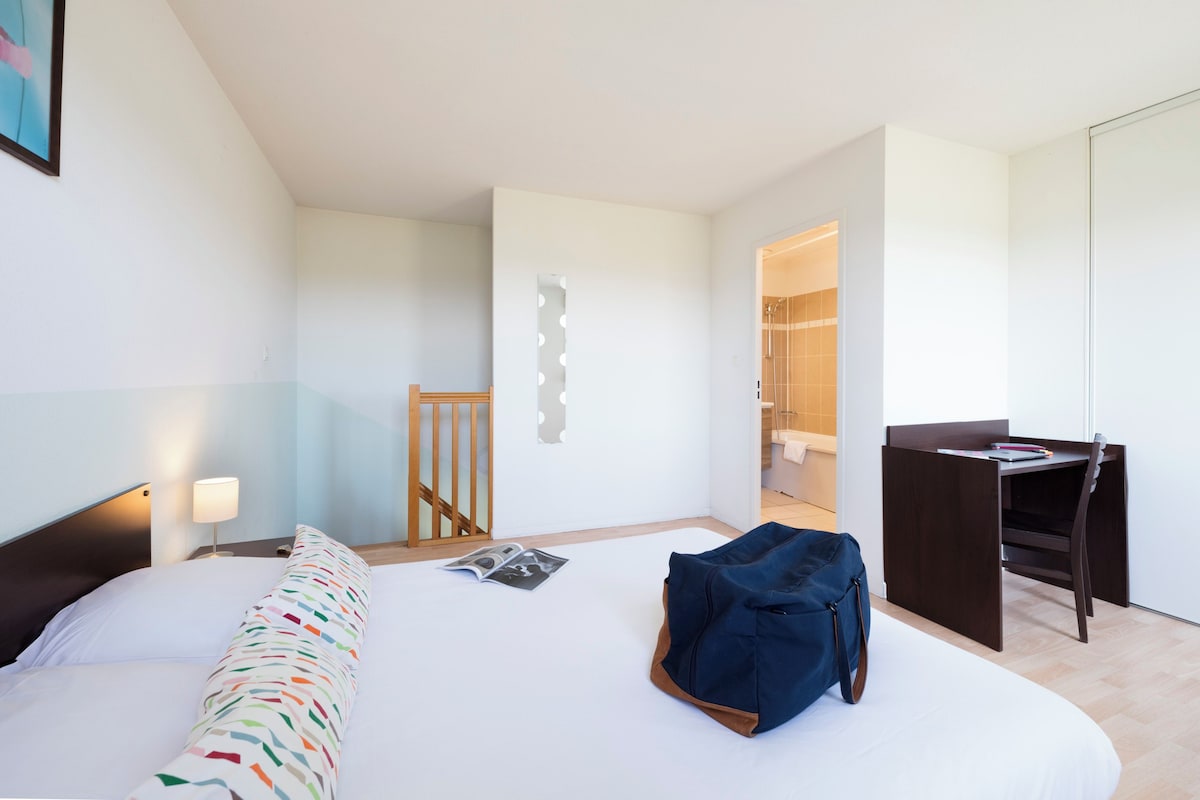 A modern hotel room with a bed, a desk, and a shower area.