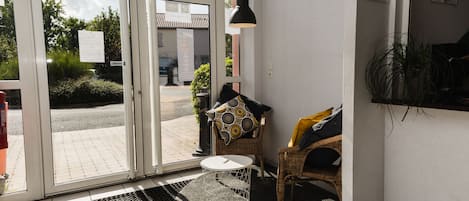 Η είσοδος ενός ξενοδοχείου με μια γυάλινη πόρτα, μια καρέκλα από μπαμπού, ένα μικρό στρογγυλό τραπέζι και ένα μαύρο φωτιστικό οροφής.