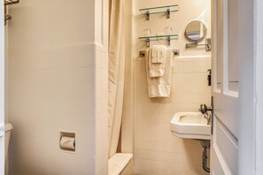 Casa de banho com sanita, chuveiro com porta de vidro, lavatório e espelho.