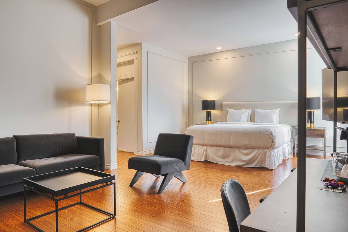 Een moderne hotelkamer met een bank, een klein tafeltje, een stoel, een bed met witte beddengoed en twee bedlampjes.