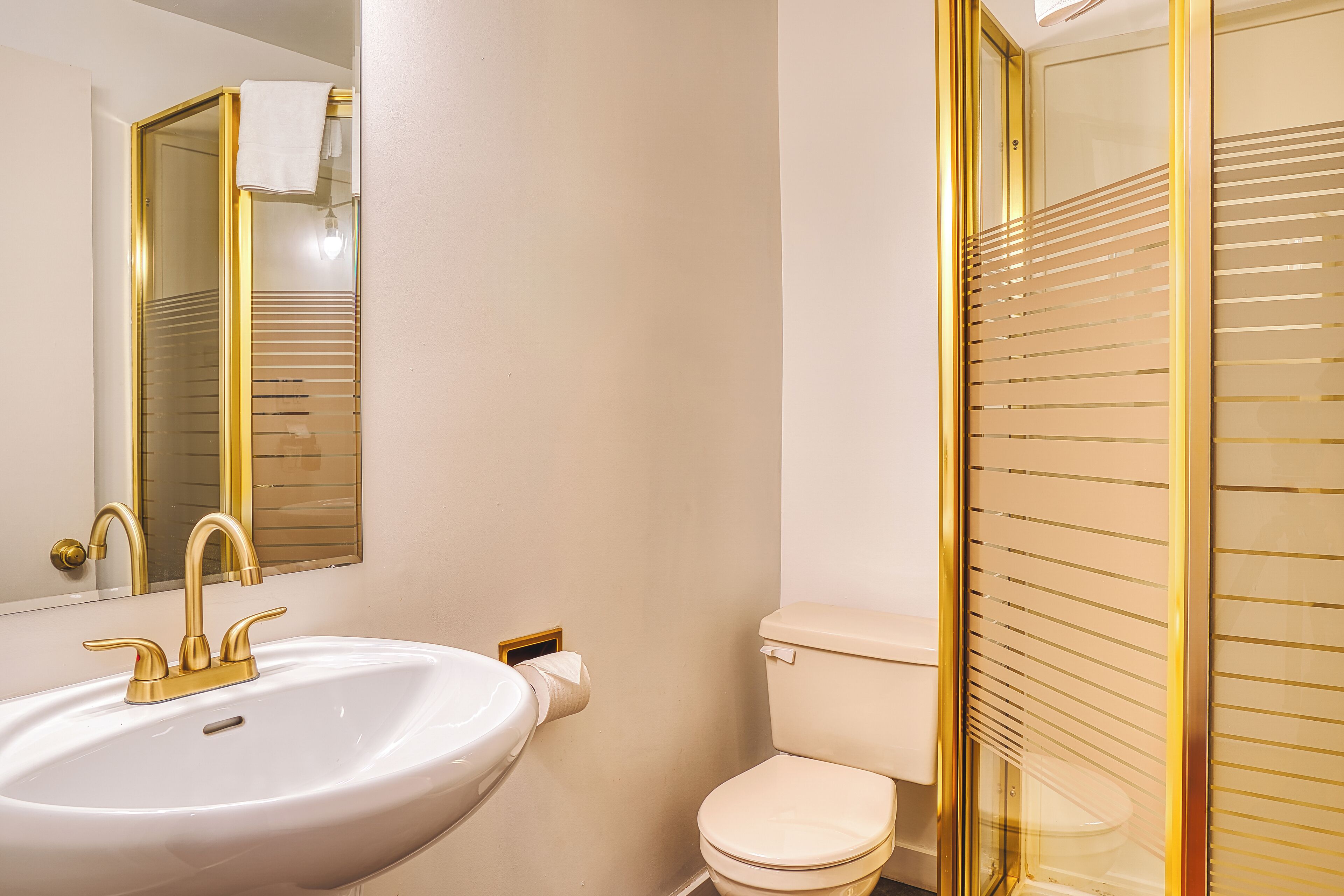 A bathroom with a white sink, gold faucets, a toilet, and a mirror with a gold frame.