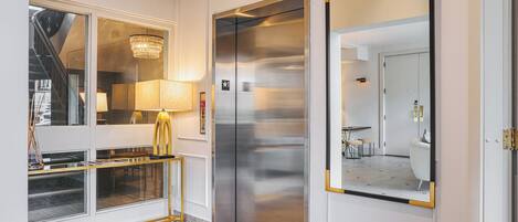 A modern elevator with a metallic finish, a glass door, and a small sign above it.