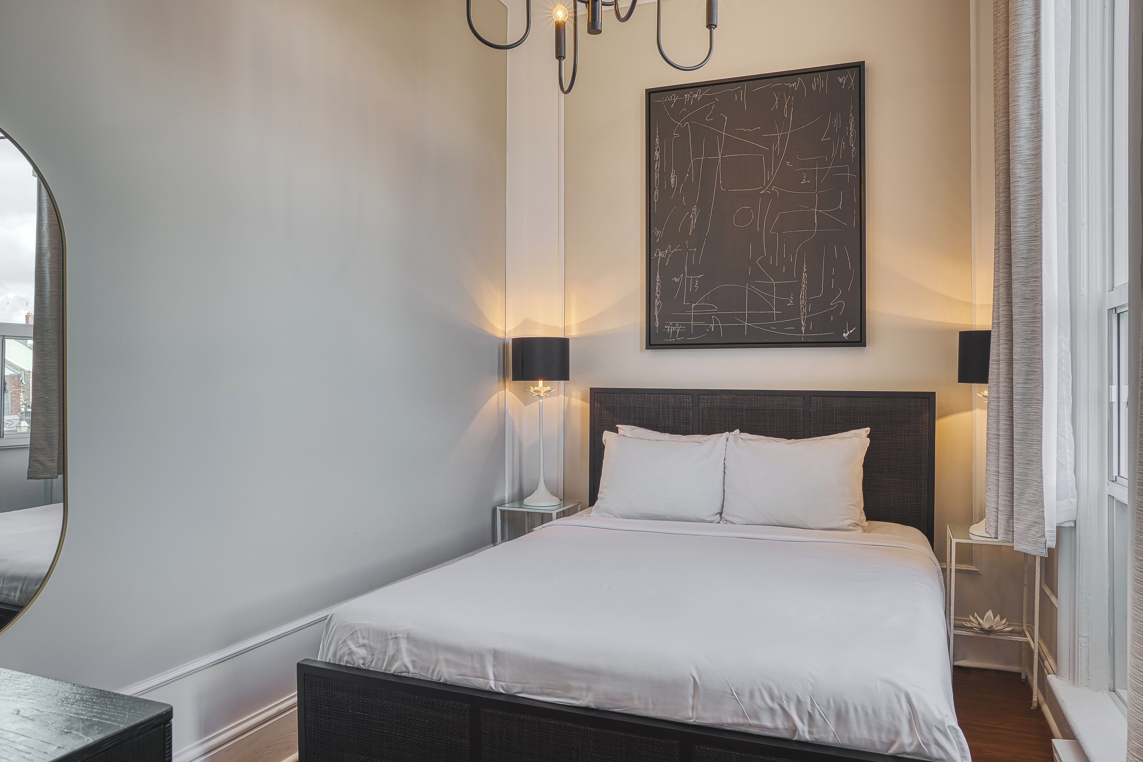 A neatly arranged bedroom with a large bed, bedside lamps, a wall-mounted abstract artwork, and a window with curtains.