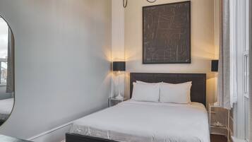 A neatly arranged bedroom with a large bed, bedside lamps, a wall-mounted abstract artwork, and a window with curtains.