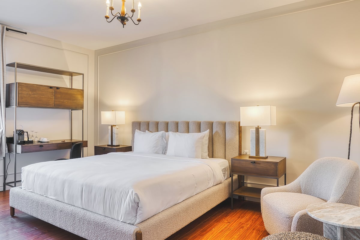 Een hotelkamer met een groot bed, twee nachtkastjes met lampen, een stoel, een bureau met stoel en een kledingkast.