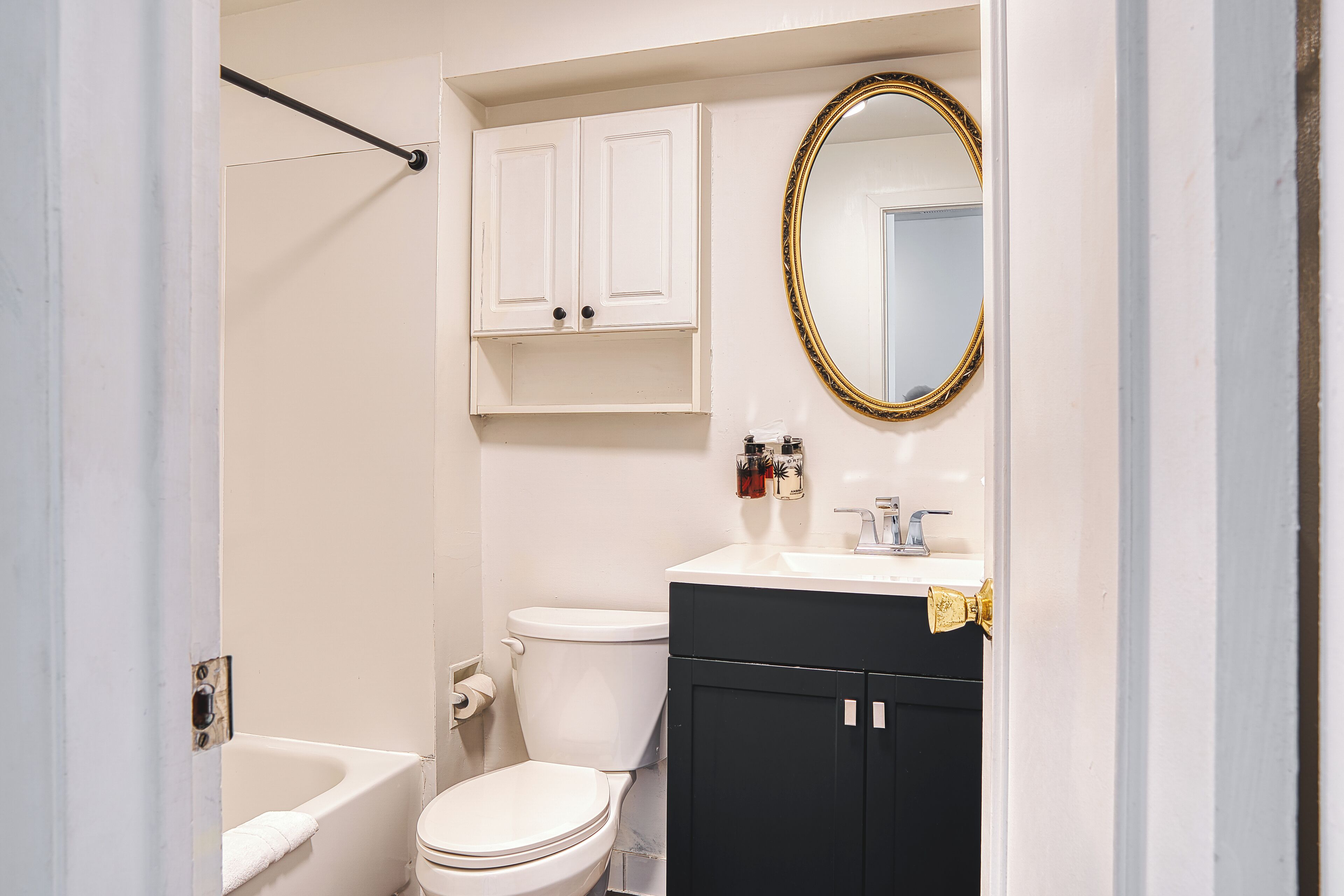 A bathroom with a white bathtub, a white toilet, a black vanity with a gold faucet, and a mirror with a gold frame.