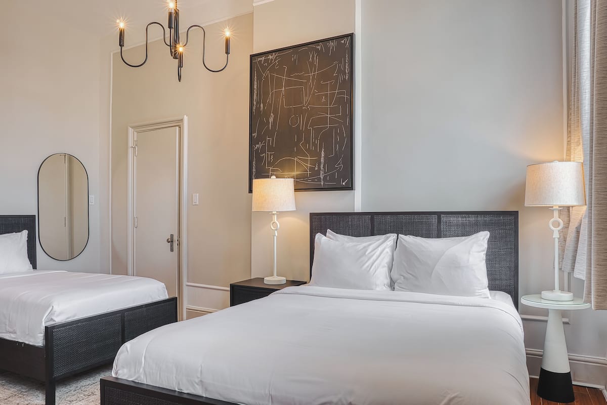 Een hotelkamer met twee bedden, een groot abstract schilderij, een kroonluchter en een ronde spiegel.