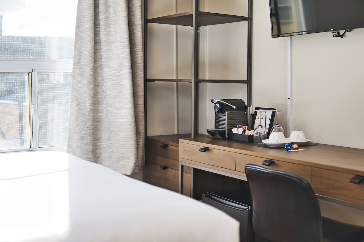 Hotelkamer met een houten bureau, een stoel, een aan de muur bevestigde televisie en een raam met uitzicht op de stad.