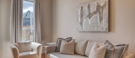 Una sala de estar con un sofá, un sillón, una mesa de centro y un cuadro abstracto grande en la pared.
