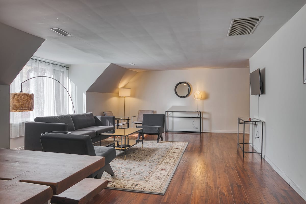 Een moderne woonkamer met een bank, stoelen, een salontafel, een vloerkleed, een televisie en een lamp.