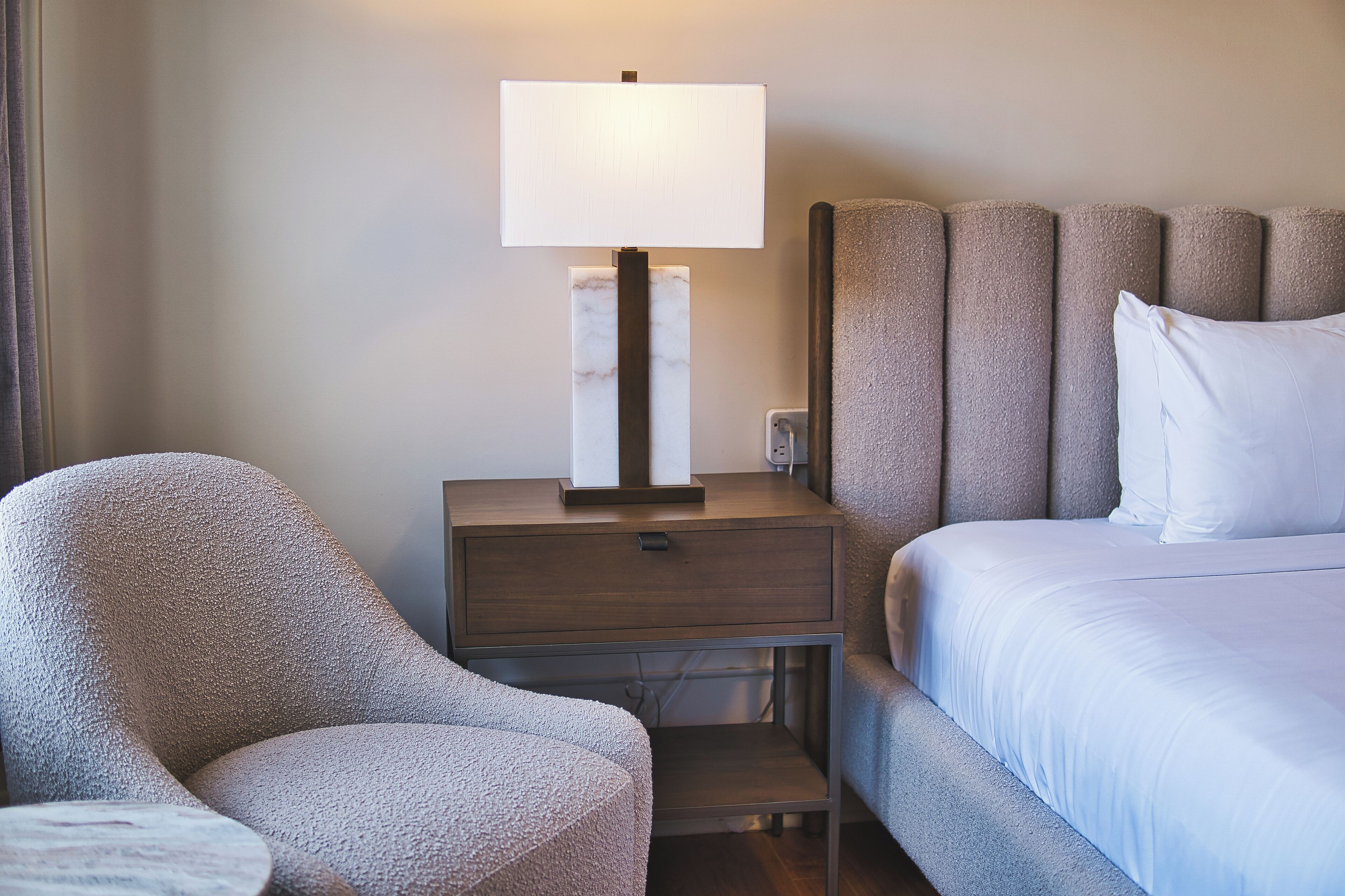 Una habitación de hotel con cama, mesita de noche con lámpara y una silla.