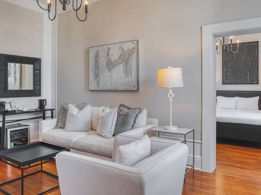 A modern living room with a sofa, coffee table, and a lamp. There is a bed with a headboard and a painting on the wall.